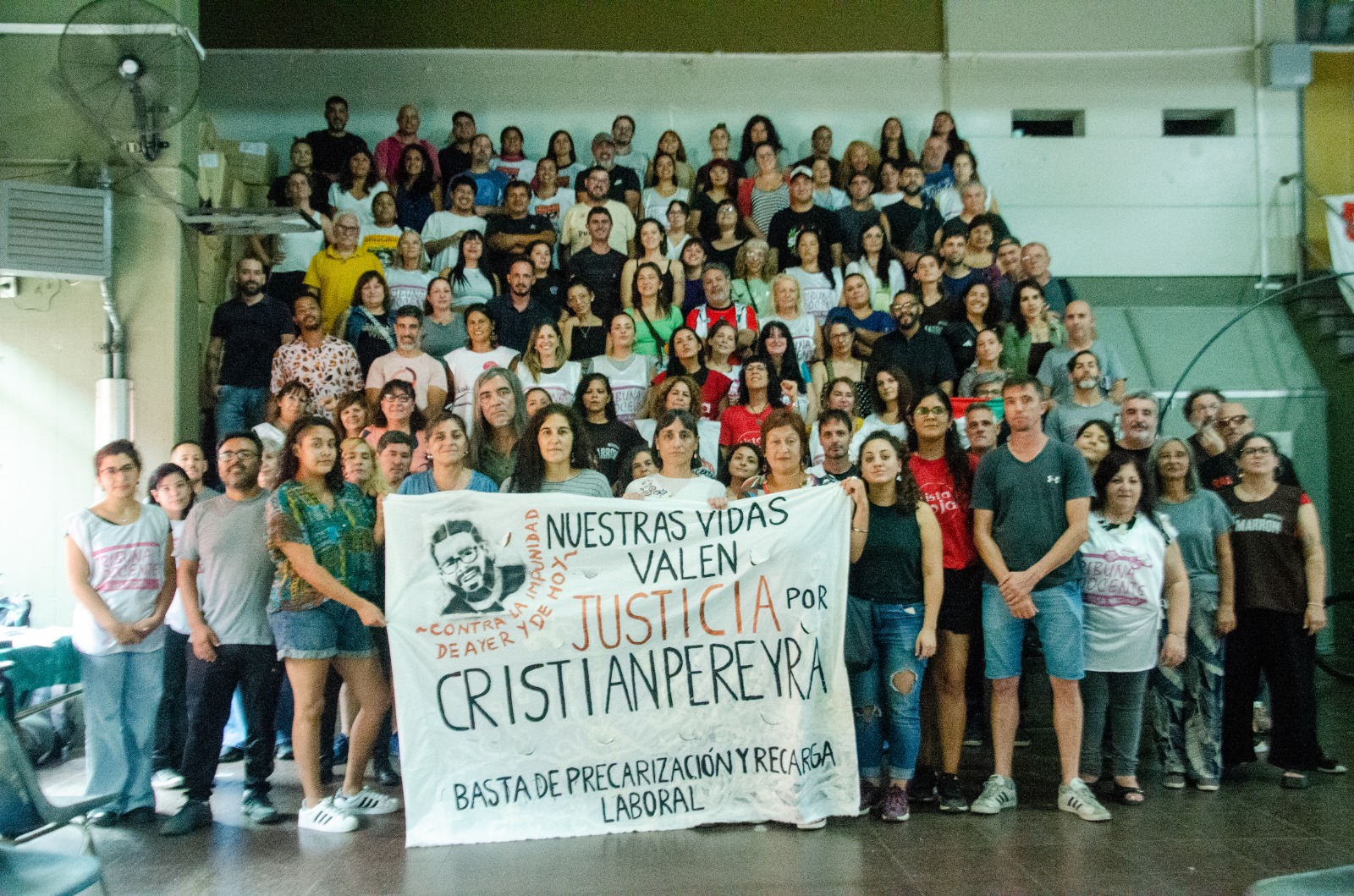 Gran asamblea de docentes con cartel de Justicia por Cristian Pereyra en un auditorio